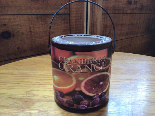 Candle in a decorative container labeled 'Cranberry Orange' on a wooden surface.
