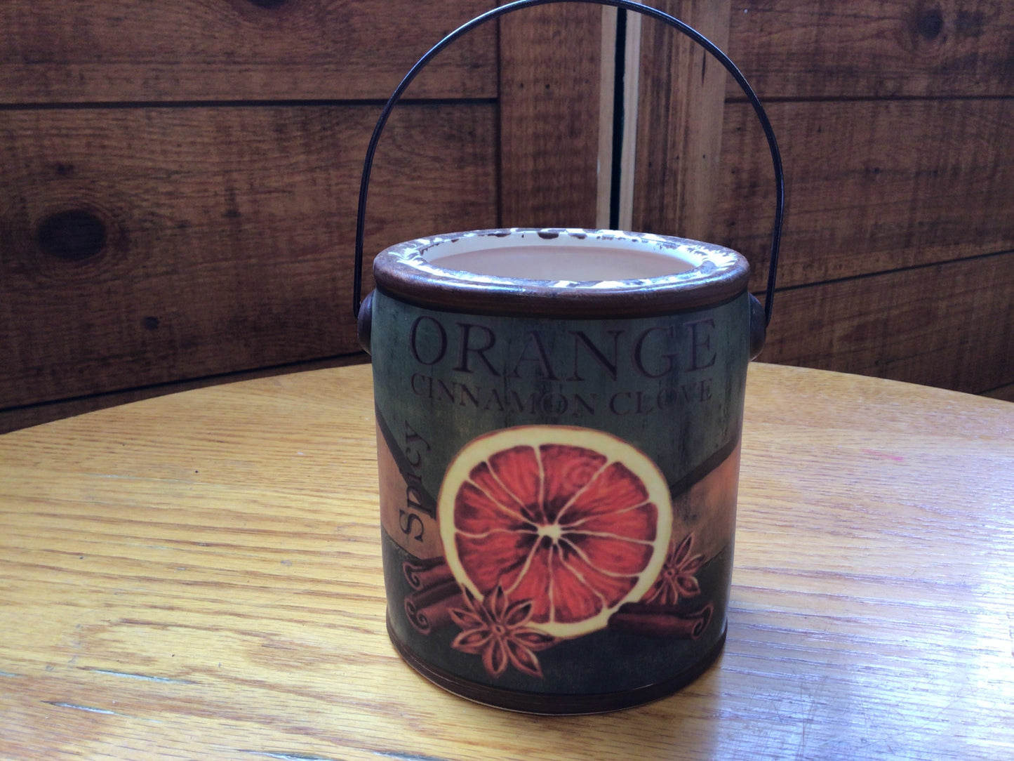 Candle container with 'Orange' text and decorative elements on a wooden surface.