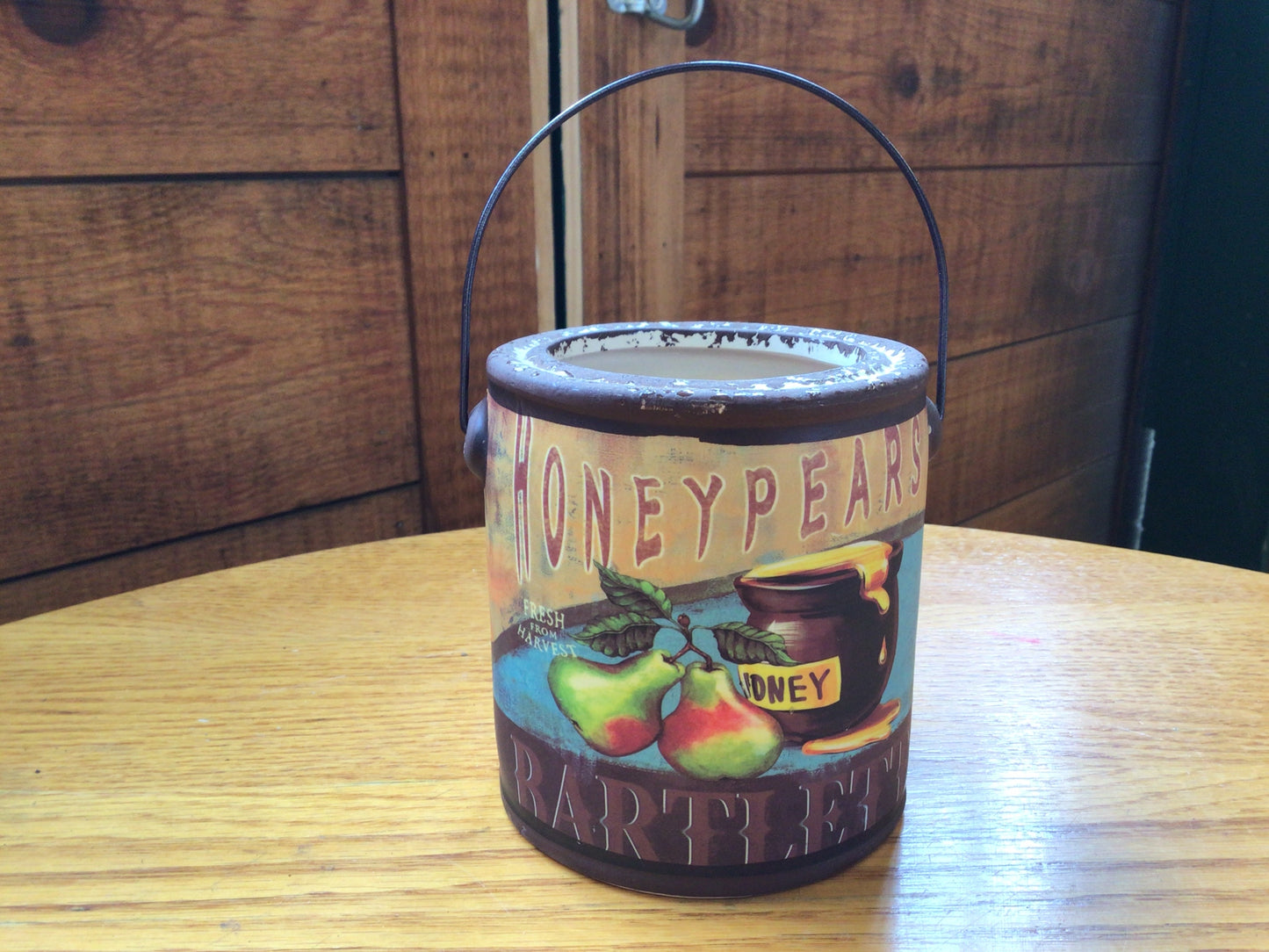 Decorative candle container labeled 'Honeypears' on a wooden surface with a wooden background.