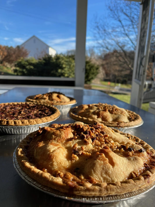 Four pies on a table with a window view of trees and a house.